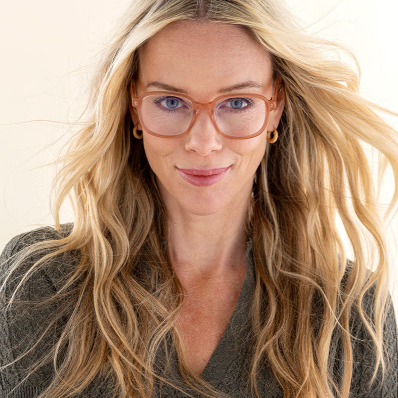Woman with long blonde hair wearing the small Eyeknow glasses in a warm translucent shade, styled with a natural look.