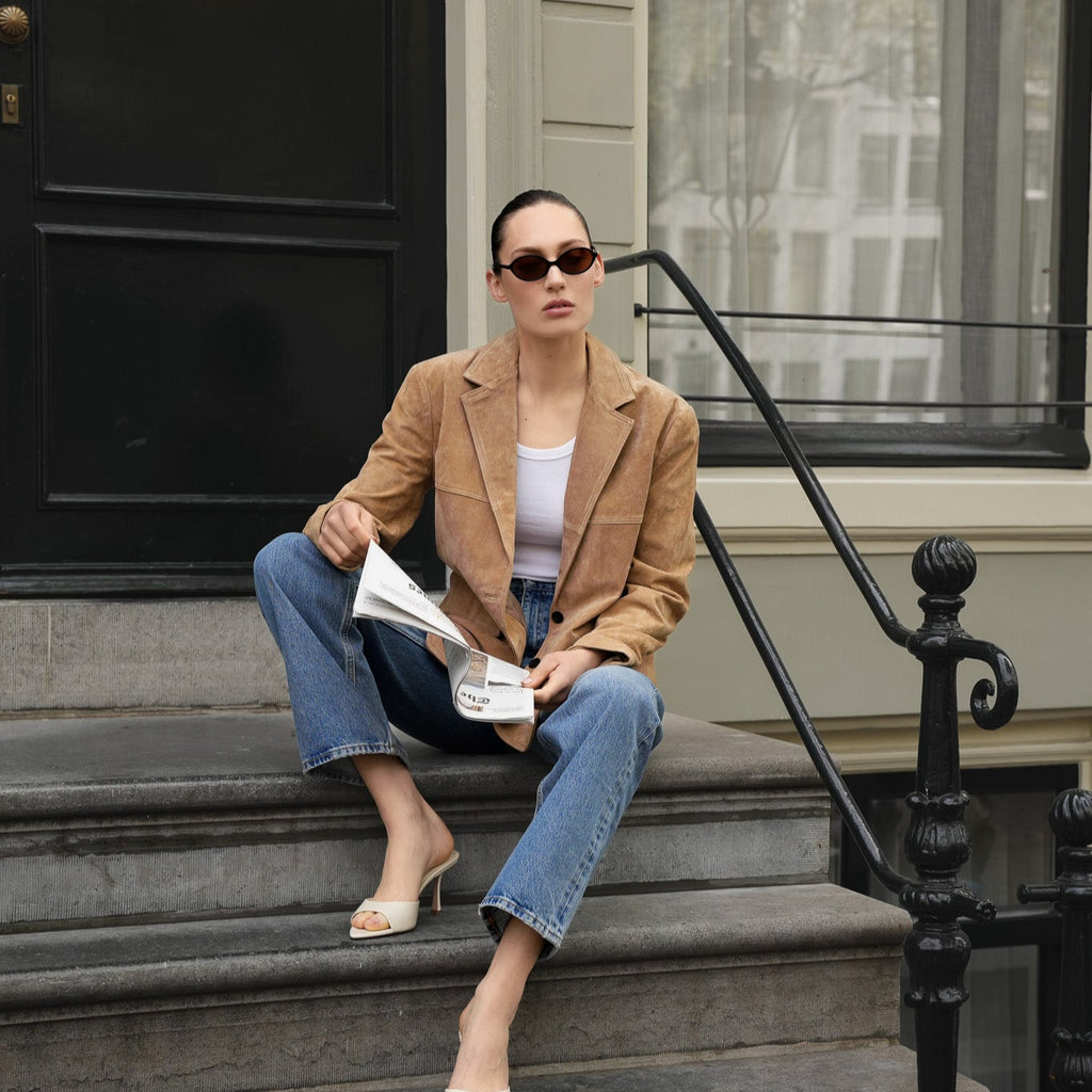 Stylish woman wearing The Eyedoll sunglasses by Frank and Lucie, sitting on city steps with a newspaper